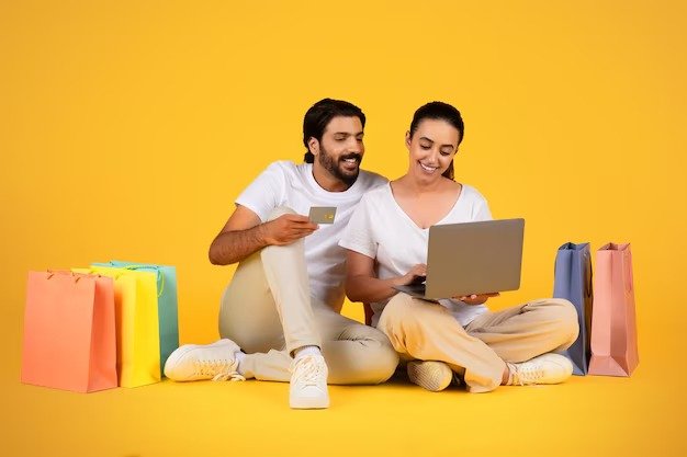 imgi 194 smiling millennial arab husband show credit card wife use laptop sit floor with many bags wi